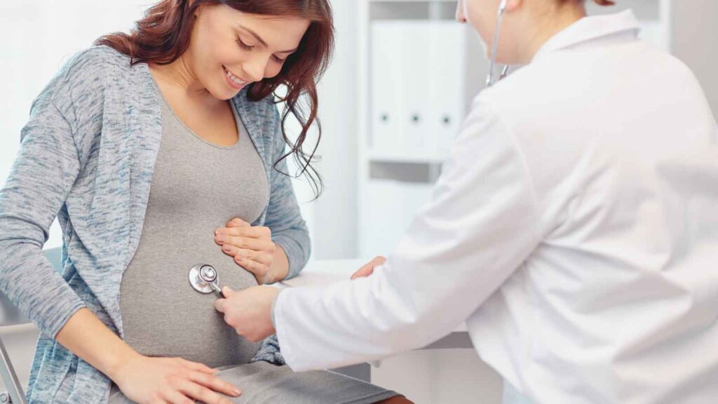 Pregnant woman smiling during prenatal testing consultation with healthcare provider using stethoscope in medical office 